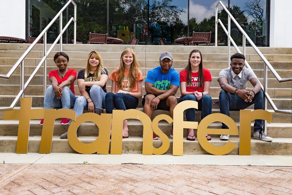 Diverse students sitting on steps smiling behind gold letters that spell T R A N S F E R, Joliet Junior College